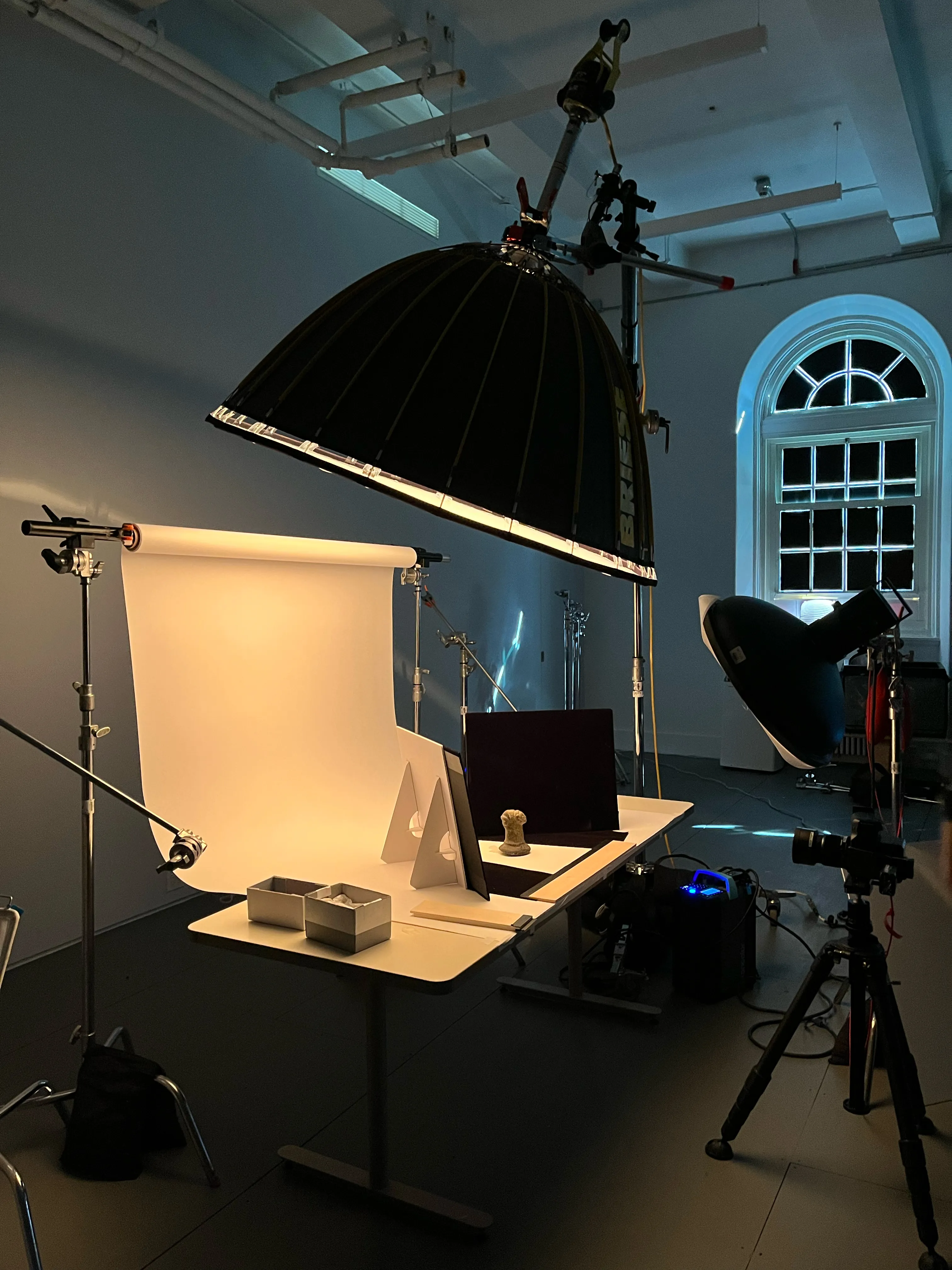 A tabletop set under a large Briese light, camera on the tripod, in a studio with arched windows.
